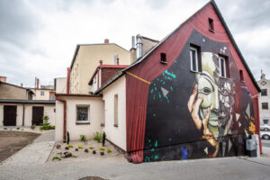 Mural na ulicy Piłsudskiego. Pod kurtyną ręka trzymająca maskę.