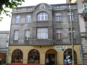 Kamienica przy ul. Piłsudskiego 42 z roku 1912. Na parterze meblowy sklep firmowy z żółtym kolorem elewacji. Kolejne piętra zajmują mieszkania z elewacją w kolorze szarym.