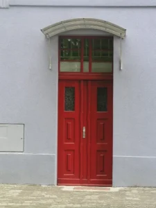 Wejście do budynku z czerwonymi drzwiami oraz zadaszeniem.